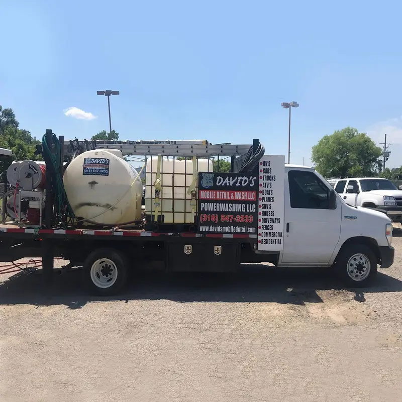 The mobile power washing rig with water tanks and hose reels, branded signage across the back