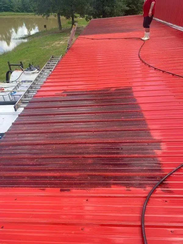 A red metal roof part-way through a soft wash, algae staining lifting off