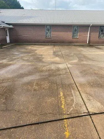 A brick building's parking lot and patio, part cleaned and part still stained