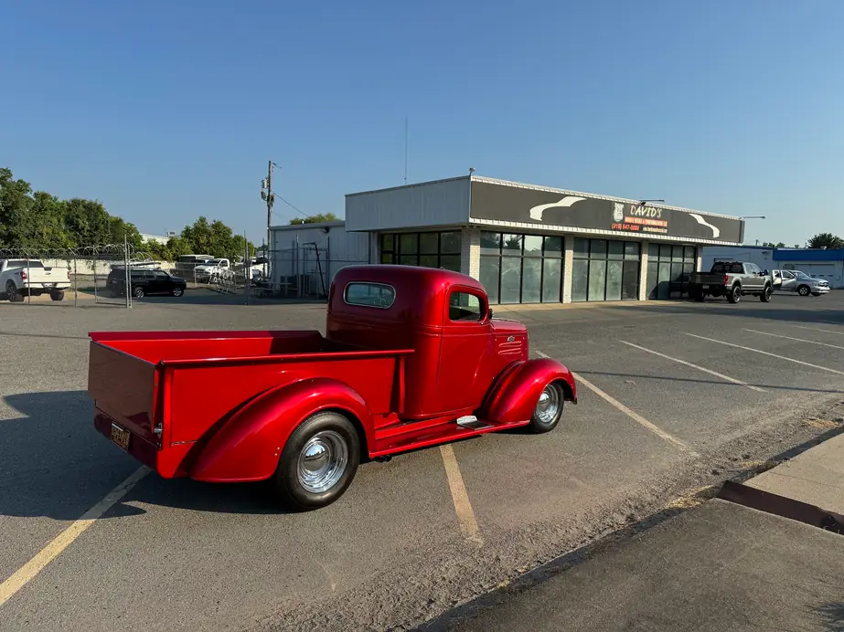 A classic red hot-rod pickup, freshly detailed, parked in front of the shop
