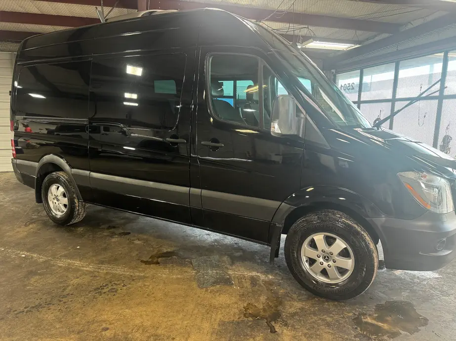 A freshly detailed black Mercedes Sprinter van inside the shop bay