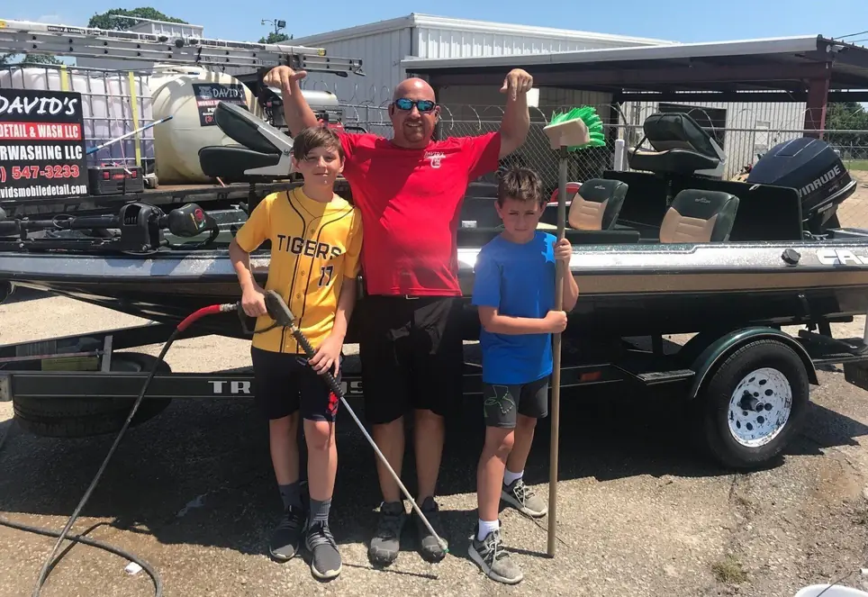 Owner David Aron with his two sons at the shop, standing beside a boat on a trailer